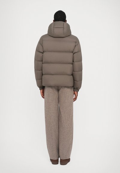 Brown puffer jacket with a high collar and elastic cuffs, paired with light brown textured wide-leg pants, viewed from the back.