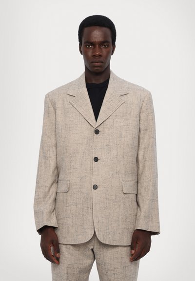 Světlý béžový blazer s texturovanou tkaninou, klopovými límci a třemi černými knoflíky. Obsahuje dvě přední kapsy a volný střih.
