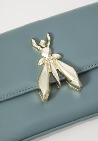 Világoskék bőr clutch, elülső részén fémes arany rovar alakú díszítéssel, sima felülettel és precíz varrással.