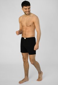 Černé bavlněné boxerky s elastickým pasem, jedním knoflíkem na zapínání a klasickým střihem. Materiál vypadá měkce a prodyšně.