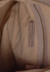 Helle beige Stoffinnenseite einer Tasche mit sichtbarem Reißverschluss und einem Etikett mit der Aufschrift "LIEBESKIND." Weiche Textur und einfaches Design.