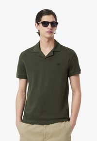 Olivgrön polo skjorta av mjukt tyg, med en klippt krage, korta ärmar och en liten broderad logotyp på bröstet.