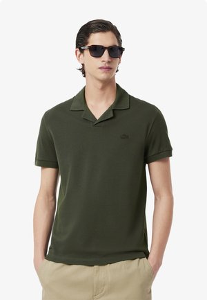 Polo shirt verde oliva realizzato in tessuto morbido, dotato di colletto a punte, maniche corte e un piccolo logo ricamato sul petto.