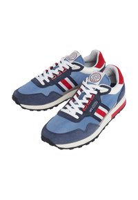 Ténis azuis e náuticos com detalhes brancos, apresentando atacadores brancos, riscas vermelhas e um emblema redondo na lingueta. Sola de borracha, materiais de camurça e tecido.