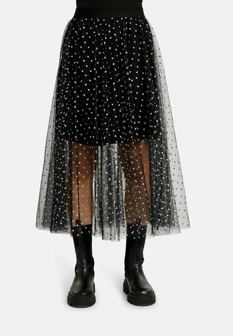 Čierna sukňa z tüllu so striebornými vzormi srdca, vrstveným dizajnom a nerovným lemom. Nosí sa s čiernymi členkovými topánkami.