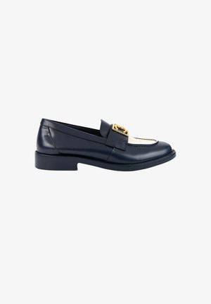 Mocassin en cuir noir et blanc avec un petit talon et une boucle décorative dorée sur la bride du dessus.