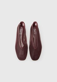 Un paio di ballerine vegan in rete di colore rosso scuro, con punta quadrata e scollatura a V profonda, esposte su uno sfondo chiaro.