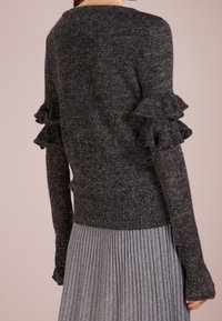 Czarny, błyszczący sweter z falbaniastymi mankietami, długimi rękawami i szerokim dekoltem. Posiada prążkowany dół oraz teksturowany, miękki materiał.