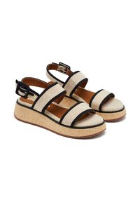 Sandalias de tela beige con correas y hebilla negras, que cuentan con una suela de plataforma texturizada y un diseño de punta abierta. Aptas para el clima cálido.