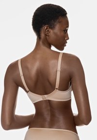 Soutien-gorge beige avec des bretelles réglables, design sans couture et texture lisse. Fermeture à crochets visible à l'arrière avec un minimum de détails.