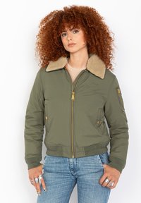 Giubbotto bomber verde oliva con colletto in pelliccia sintetica beige, chiusura frontale con zip, due tasche laterali e una tasca con zip sulla manica. Tessuto liscio, design aderente.