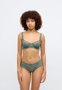 Conjunto de lingerie verde em renda, incluindo um sutiã balconette com detalhes bordados e uma tanga hipster correspondente com bordas recortadas e detalhes decorativos.