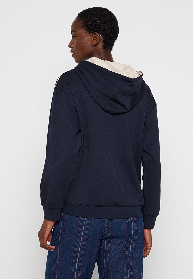 Navy sweatshirt met een capuchon, voorzien van een beige binnenvoering. Losse pasvorm met geribde manchetten en onderrand. Glad stoffen textuur, eenvoudig ontwerp.