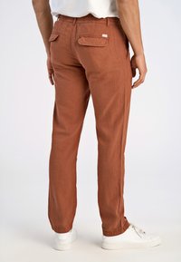 Bruine, lichte broeken met een elastische tailleband, twee achterzakken en taps toelopende pijpen, gecombineerd met witte sneakers.