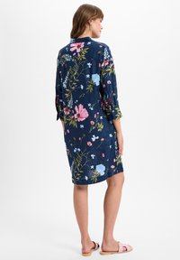 Floral Shirtkleid mit kurzen Ärmeln aus dunkelblauem Stoff, das lebhafte Muster in Pink, Blau und Grün zeigt. Lässiger Schnitt, seitliche Schlitze, knöchellang.