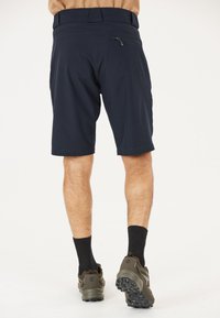 Marinblå shorts med en avslappnad passform, dragkedjeficka på baksidan och en mjuk textur, även i kombination med mörka strumpor och skor.