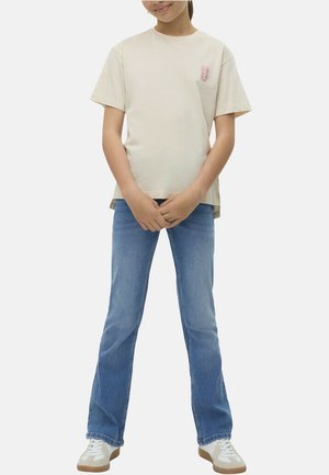 T-shirt beige à manches courtes avec un col rond et un petit graphique sur la poitrine gauche ; associé à un jean flare bleu clair.