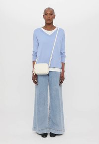 Light blue long-sleeve top over a white tee, paired with wide-leg light denim jeans. A small cream crossbody bag completes the outfit.