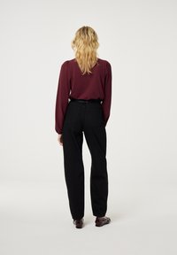 Bordeaux langemouw blouse met elastische manchetten, gecombineerd met hoge zwarte broek. Heeft een stevige textuur en een minimalistisch ontwerp.