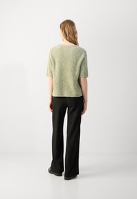 Green fuzzy short-sleeve sweater with a relaxed fit, paired with black wide-leg trousers and flat black shoes. Simple design, soft texture.