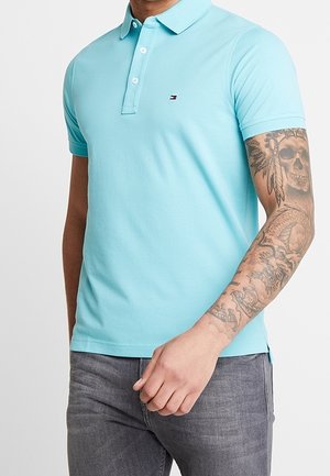 Polo bleu clair en coton, doté d'un col classique et d'une patte à deux boutons. Comprend un petit logo sur le côté gauche de la poitrine.