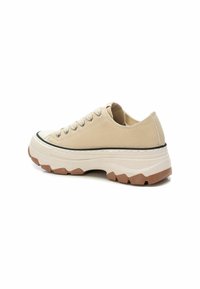 Zapatillas bajas beige con parte superior de lienzo texturizado, suela de goma y ribete negro a contraste. Cuentan con cordones redondos y una suela de patrones gruesos.