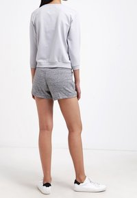 Šedá mikina s tříčtvrtečními rukávy a zpevněným výstřihem, v kombinaci se šedými šortkami. Bílá tenisky dokončují outfit. Hladká textura, volný střih.