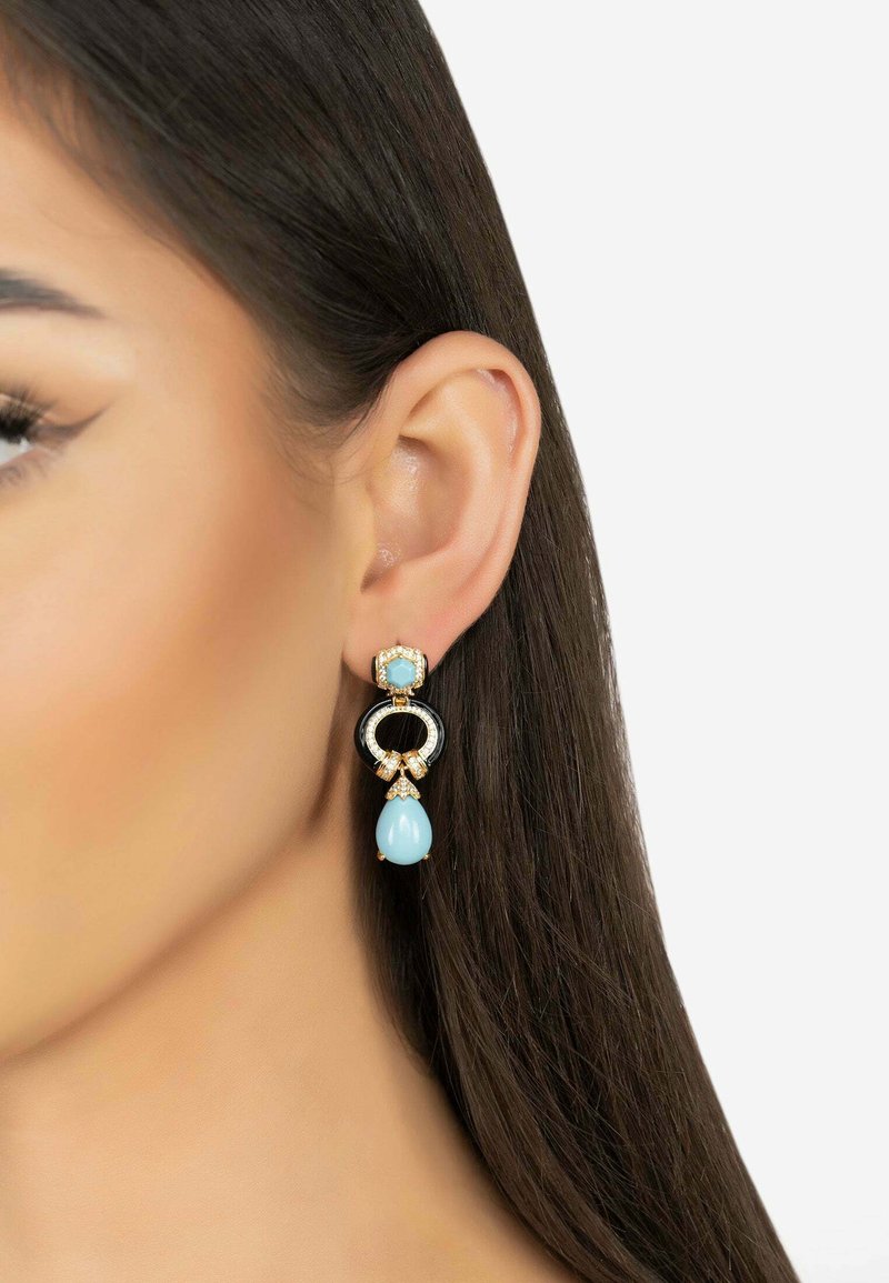 Pendientes en tono dorado con un diseño circular negro, adornados con un colgante de gota azul claro y acentos de piedras preciosas transparentes.