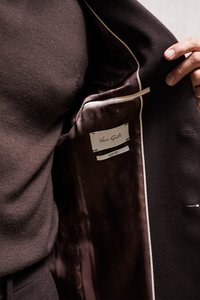 Main tenant une veste de costume slim Van Gils marron foncé ouverte, révélant la doublure intérieure et l'étiquette de la marque.