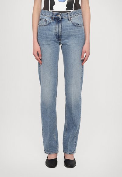 Jean droit bleu clair avec une finition délavée, design à cinq poches et passants de ceinture, porté avec un t-shirt graphique noir et blanc.