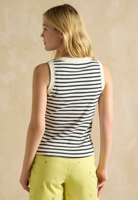 Námornícka a biela pruhovaná tielko bez rukávov s okrúhlym výstrihom a mäkkou tkaninou. Nosené s svetložltými nohavicami s malými vyšívanými detailmi.