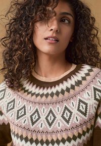 Pull en tricot avec un motif géométrique rose, blanc et marron. Col rond avec un bord côtelé contrasté. Tissu doux et texturé.
