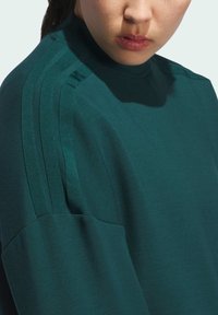 Maglione lungo verde scuro con maniche lunghe e colletto alto, caratterizzato da tre strisce verticali lungo le spalle, realizzato in un tessuto liscio e morbido.