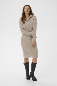 Robe beige en tricot avec texture côtes, col zippé mi-hauteur, manches longues et design ajusté. Associée à de hautes bottes en cuir noires.
