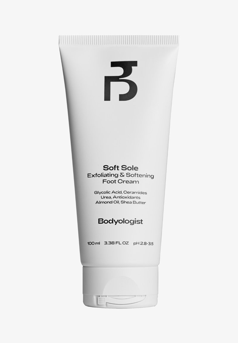 Tube en plastique blanc de crème pour les pieds, avec un logo noir, et un texte noir indiquant les ingrédients et les détails du produit. Taille de 100 ml.