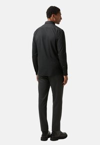 Black button-up shirt with a straight cut, paired with dark gray trousers. Features include long sleeves and a collared neck. Black footwear.