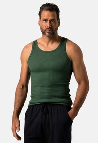 Canotta verde a costine con spalline larghe e una vestibilità aderente, abbinata a pantaloni scuri con cordoncino e tasche laterali.