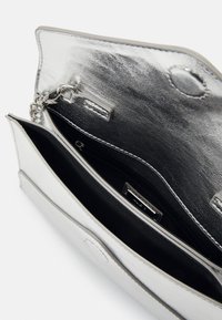 Stříbrná metalická psaníčko s hladkým povrchem. Obsahuje černou podšívku, zipovou kapsu a detail z řetízku.