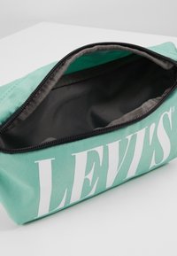 Astuccio turchese realizzato in tessuto resistente, dotato di una ampia zip di apertura e di un audace logo bianco "LEVI'S" su un lato. L'interno è di colore nero.