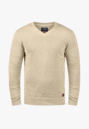 Svetr béžové barvy s výstřihem do V a dlouhými rukávy, vyrobený z měkkého pleteného materiálu. Má žebrované manžety a lem, s malým logem na spodní části.