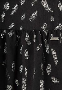 Tejido negro con un patrón salpicado de plata, que presenta una superficie texturizada y un dobladillo con volantes. Incluye una pequeña etiqueta de logo.
