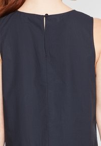 Top sin mangas de color marino con una abertura en la espalda en forma de llave, textura suave y un diseño sencillo con detalles de costura mínimos.