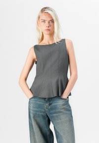 Grå ärmlös topp med båtutskärning, med vertikala veck och en utsvängd nederkant. Parat med blå vida jeans.