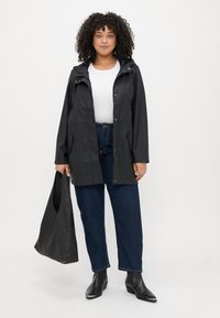 Svart vattentät jacka med huva, tryckknappar, två framfickor, matchad med mörkblå jeans och svarta ankelboots, bär en svart tote-väska.