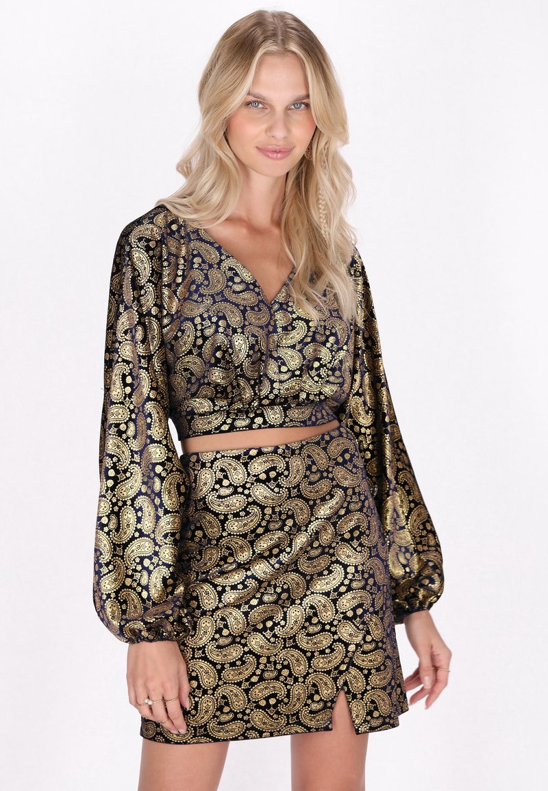 Czarny i złoty top z krótkim rękawem w wzór paisley oraz pasująca spódnica. Materiał ma błyszczącą teksturę z misternymi złotymi detalami i rozcięciem u dołu.