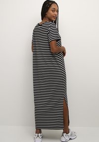 Black and white striped maxi dress with short sleeves, side slits, and a relaxed fit, paired with gray sneakers.