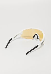 Weiße Sportsonnenbrille mit gelb getönten Bogenlinsen und schwarzen Gummi-Griffen an den Bügeln und am Nasensteg.