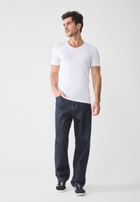 White short-sleeve t-shirt paired with dark blue denim jeans. Shoes are black with white soles. The fit is casual and relaxed.