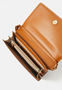 Brun handväska i läder med en mjuk textur, utrustad med ett guldspänne, flera fack och ett kontrasterande beige inre.