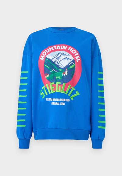 Sweatshirt azul com um gráfico redondo contendo o texto "Hotel da Montanha", montanhas e riscas verdes nas mangas. Material em mistura de algodão.
